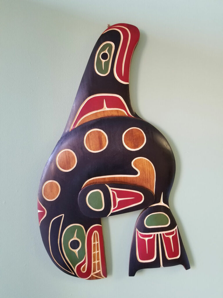 John Patrick Spence carving of a whale, carving, hanging on a wall, in green, red, black and natural wood colours
